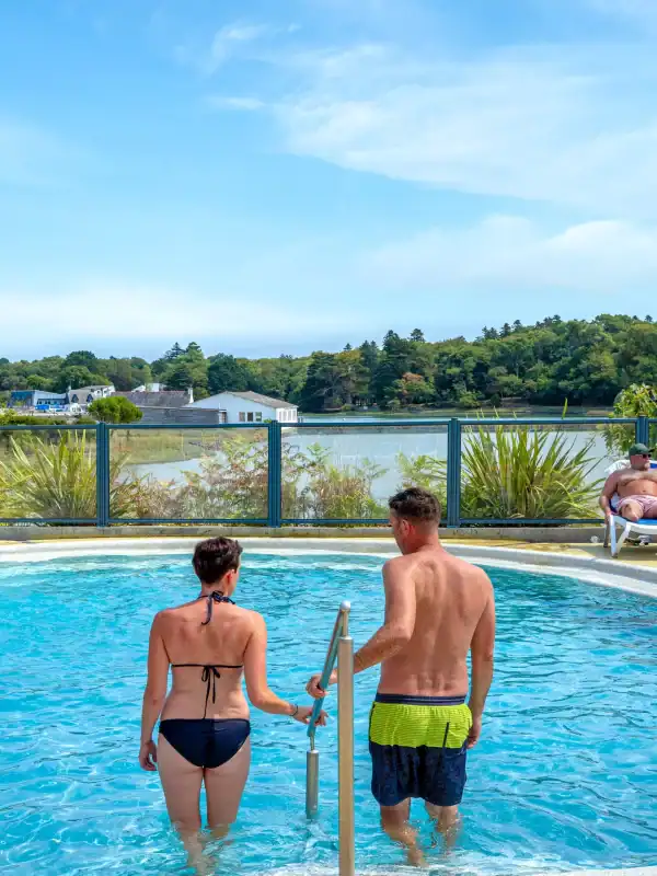 Ein Paar im beheizten Pool eines Campingplatzes am See – ein Moment der Entspannung und des Urlaubs